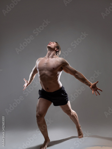 Muscular man in an artistic pose, portrait on a gray background. The guy is an athlete with spectacular muscles posing with his arms outstretched