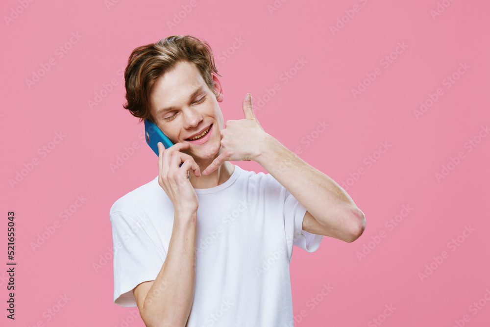 handsome, pleasant, smiling young man holds a smartphone near his ear and shows a handsome, pleasant, smiling young man holds a smartphone near his ear and shows a