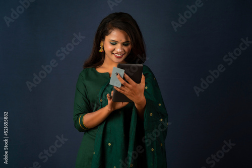 Young smiling beautiful woman or girl presenting credit card while using mobile or smartphone.