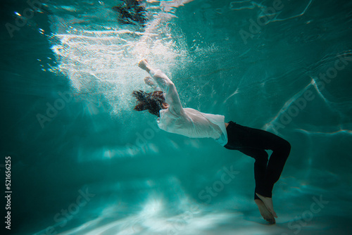 Beautiful underwater shooting  guy in white shirt and pants has fallen under the water and drowning. go to bottom  concept. young man paddles with his hands under water  waves and splashes around him