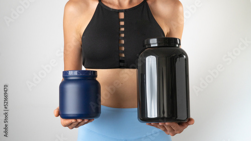 Athletic slender woman holding cans of protein and sports supplements for an effective workout in the gym