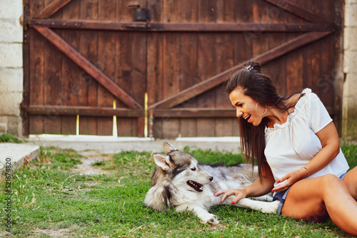  Woman and Dog.Smiling Beautiful Woman having fun and hugging cute siberian Husky Dog at the back Yard . Woman Playing with her dog durign the summer vacation 