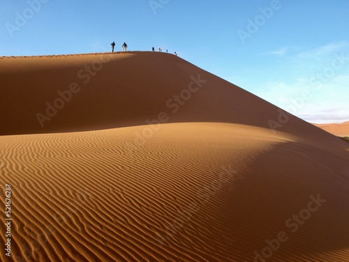 Huge big orange yellow sand dune in the desert in Namibia Africa with blue sky background and shadows on the sand walking tour expedition adventure group on top of dunes and footprints 