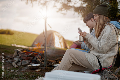Caucasian females sitting at fire in camp site and using phones when resting. Travelers.