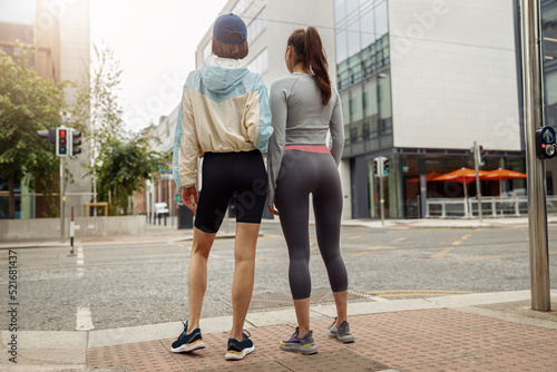 Two sportive young female friends walking city after morning running. Back view