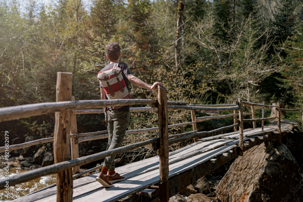 Rear on man traveler with backpack standing on bridge over river in forest. Traveling concept. Rear on man traveler with backpack standing on bridge over river in forest. Traveling concept.