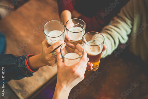 Young people celebrating with beers toasting at the irish pub - closeup crop shot of hands holding beer glasses clinking over the pub\'s table - friendship and alcohol lifestyle concept