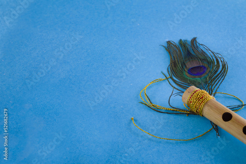Bamboo flute decorated with peacock feather symbolic to hindu god lord krishna during celebration of janmashtami festival. photo taken in blue background with copy space.