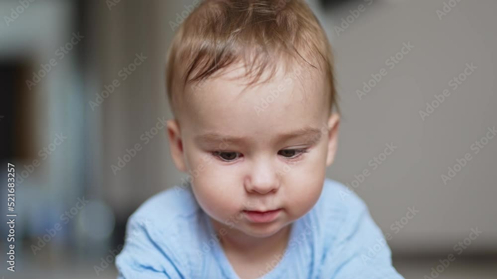 Calm adorable baby lies on belly his face to the camera. Beautiful kid notices something and crawls to it. Close up. Calm adorable baby lies on belly his face to the camera. Beautiful kid notices something and crawls to it. Close up.