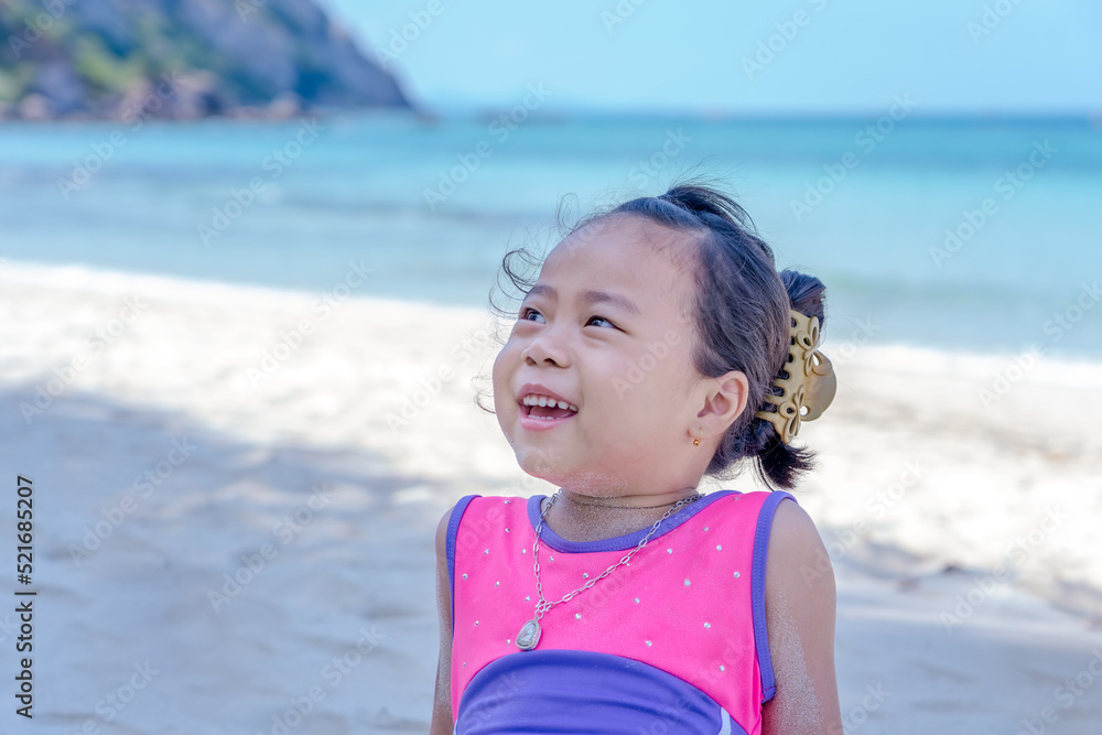 Close-up of a little Asian girl looking and smiling on the beach during a summer vacation on the bright, cheerful, relaxed tropical coast. Close-up of a little Asian girl looking and smiling on the beach during a summer vacation on the bright, cheerful, relaxed tropical coast.