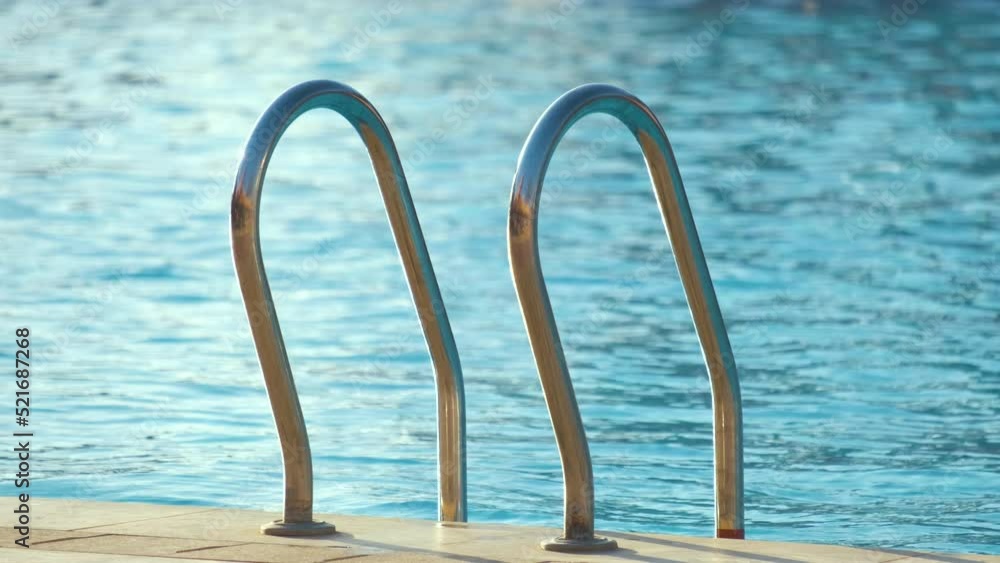 Close up of swimming pool stainless steel handrail descending into tortoise clear pool water. Accessibility of recreational activities concept Close up of swimming pool stainless steel handrail descending into tortoise clear pool water. Accessibility of recreational activities concept
