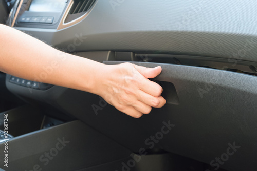 Woman opens a glove compartment in a car. The driver, sitting behind the wheel, reaches to open the glove compartment. Car interior, details.