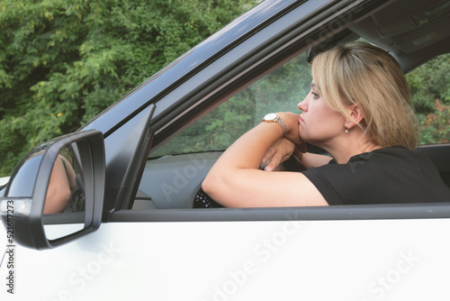 Attractive woman with blond hair put her hands and head on the steering wheel and looks forward sadly. A woman is bored in a traffic jam. Depressed business lady is sitting in the car.
