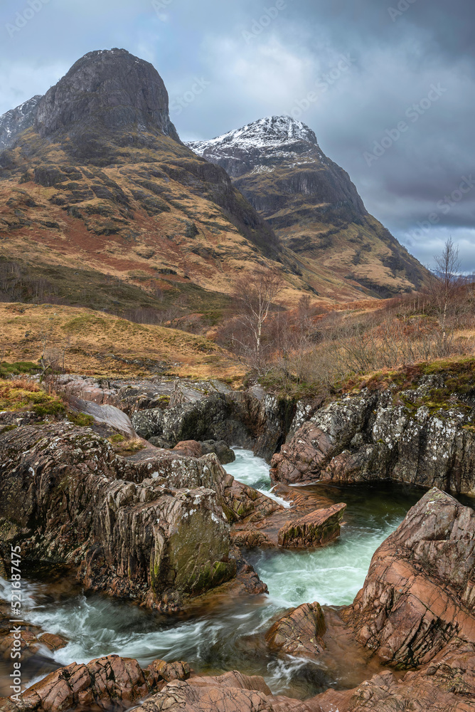 Obraz premium Gorgeous landscape image of vibrant River Coe flowing beneath snowcapped mountains in Scottish Highlands