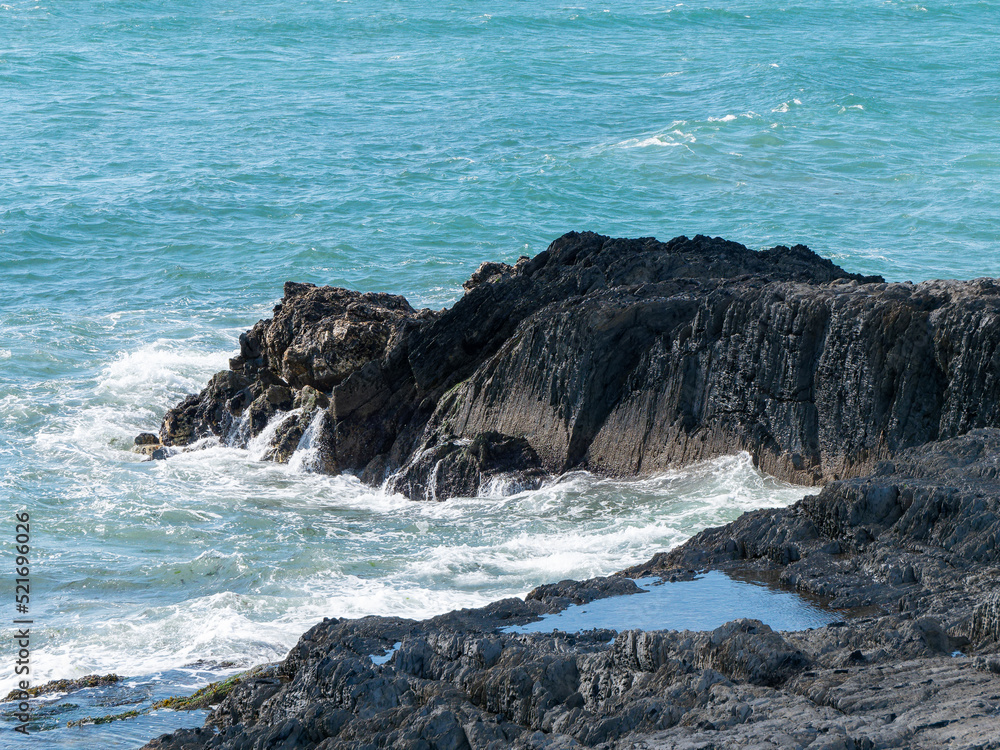 Tidal waves break on black coastal rocks, seascape. The water is turquoise in color. White foam on the waves, splashes, rock beside sea. Tidal waves break on black coastal rocks, seascape. The water is turquoise in color. White foam on the waves, splashes, rock beside sea.