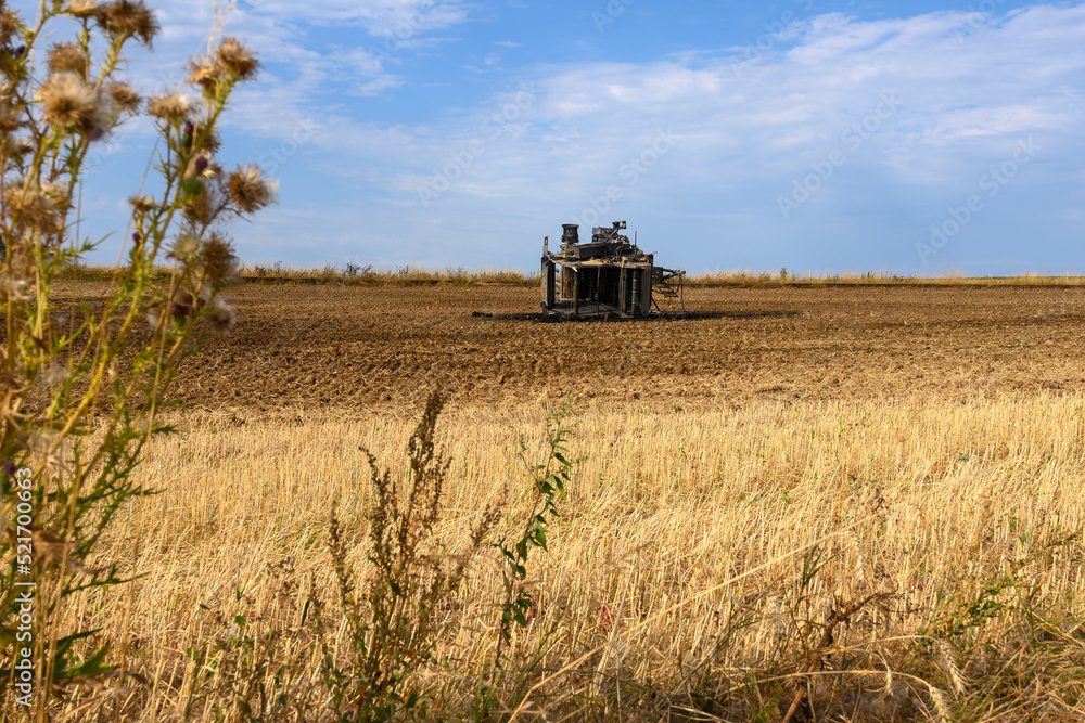 Naklejka premium A tipped over and burnt out hay baler lying in a field in summer