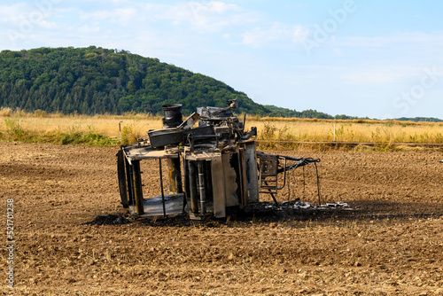 Konstfotografi Top view of a burnt out hay baler lying in a field against a green forest
