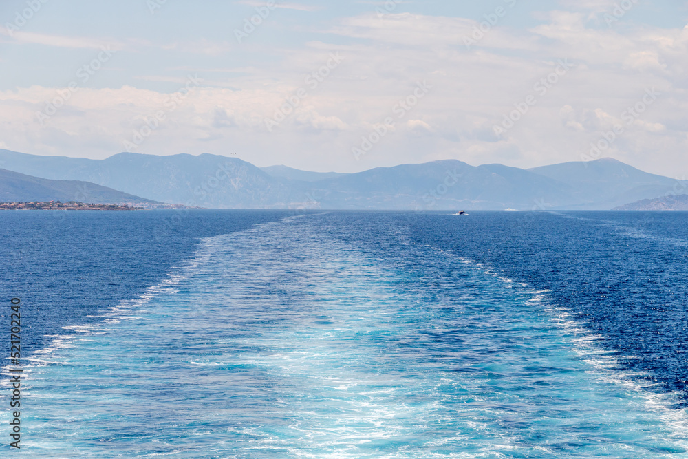 View of the water trail left by the ferry and the mountains of Greece in the background