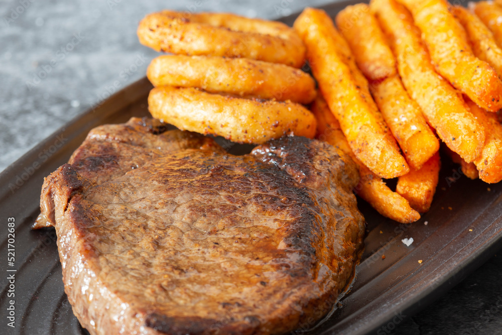 Rump steak dinner, with sweet potato fries and onion rings, on a black oval plate. On a dark stone background Rump steak dinner, with sweet potato fries and onion rings, on a black oval plate. On a dark stone background