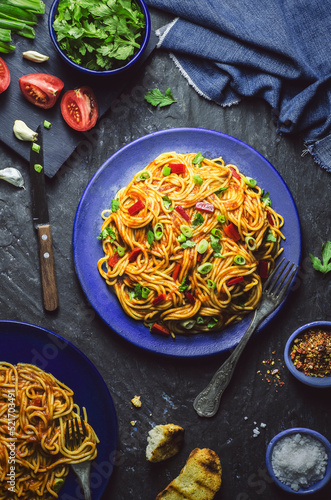 Spaghetti with tomato sauce, red pepper and green onion served with roasted bread and spices on dark background. 