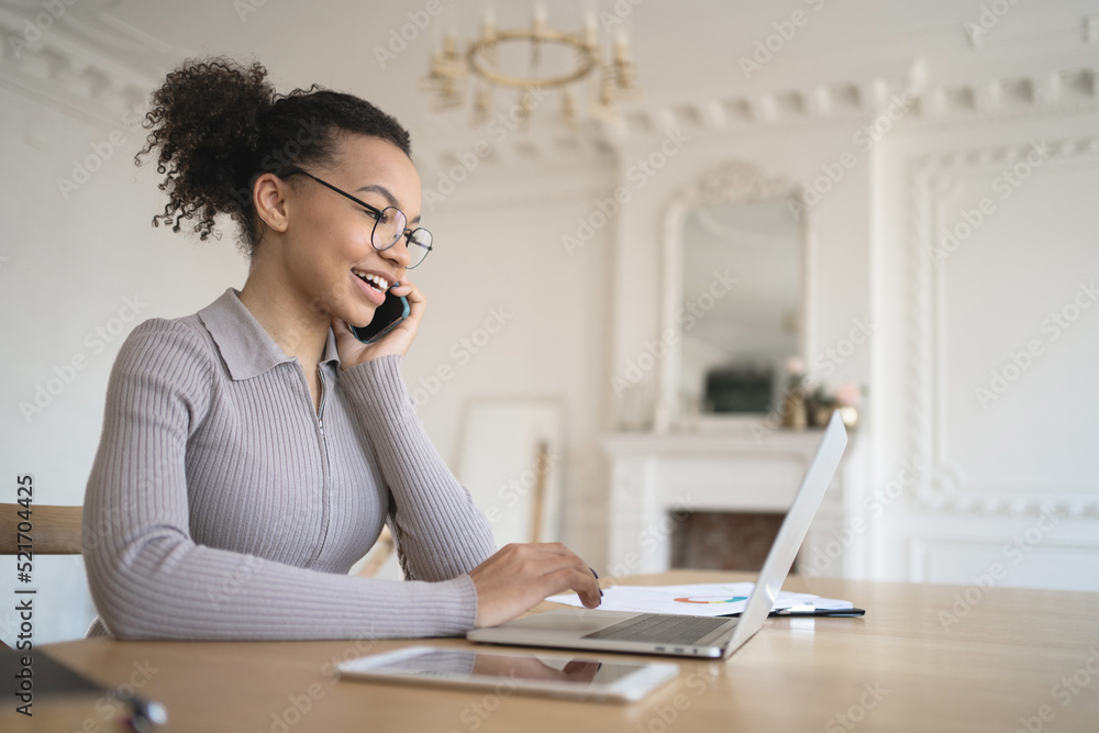 Obraz premium A female employee in the office with glasses works, uses a laptop, answers the client's mail and phone
