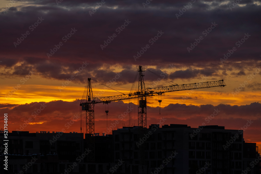 tower cranes over high-rise buildings, a new building against backdrop of sunset. Construction of apartment buildings