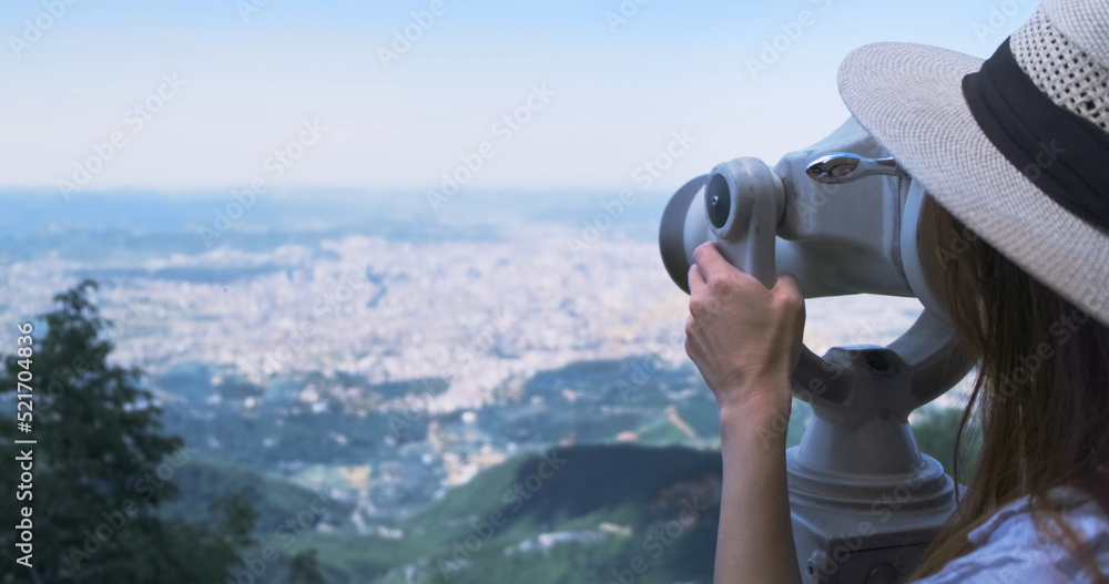 Unrecognizable woman traveler looking through viewing binoculars at summer city. Copy space. Woman in straw hat observes of blur panorama, with binoculars at observation deck. Mountain Dajti Albania