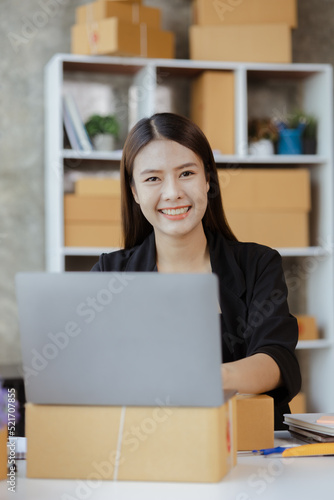 A beautiful Asian business owner opens an online store, she is checking orders from customers, sending goods through a courier company, concept of a woman opening an online business.