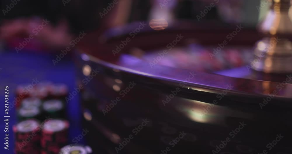 Vibrant casino table with roulette in motion, with casino chips, tokens, the hand of croupier, dollar bill money and a group of gambling rich wealthy people playing bet in the background
Vibrant casino table with roulette in motion, with casino chips, tokens, the hand of croupier, dollar bill money and a group of gambling rich wealthy people playing bet in the background