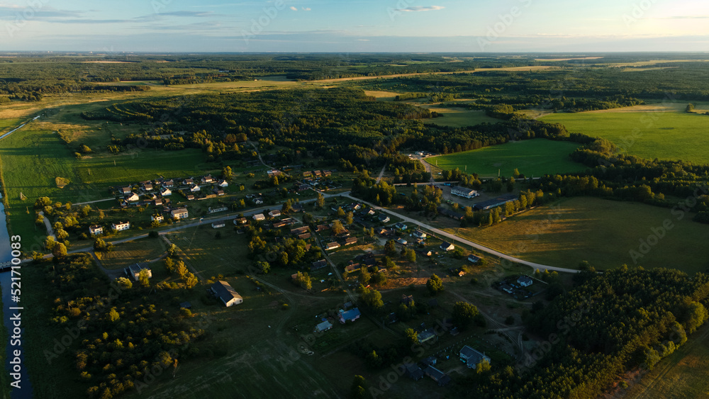 Rural landscape at sunset. Roofs of houses are visible among the trees. Aerial photography.