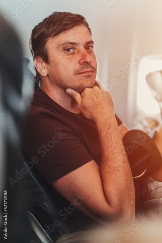 bored thoughtful unshaven people person man with 40+ years with stubble is sitting on a airplane during a flight from the airport to travel. spending time on the air plane. idle and do nothing. flare