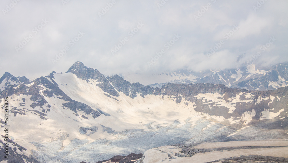 Panoramic dramatic top view in the Elbrus region of Russia - peaks of high mountains with glaciers and snow on a foggy cloudy day and a space for copying soft focus