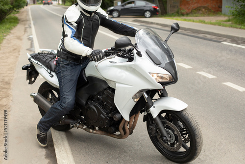 Motorcyclist takes to road. Biker on track. White motorcycle.