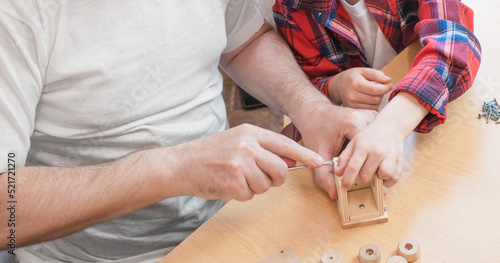 Happy father's day and childhood concept. Close-up of a father and a boy son in glasses work with hand tools, using a screwdriver, assembling a wooden house constructor at the table.