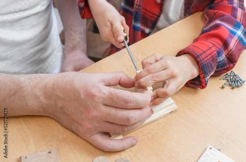 Happy father s day and childhood concept. Close-up of a father and a boy son in glasses work with hand tools  using a screwdriver  assembling a wooden house constructor at the table.