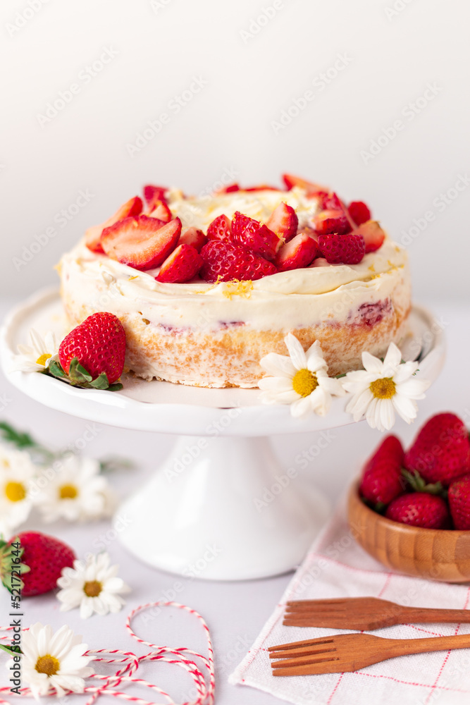 Strawberry vanilla cake on a white cake stand, whith wooden forks and strawberries and white daisies on a white background Strawberry vanilla cake on a white cake stand, whith wooden forks and strawberries and white daisies on a white background