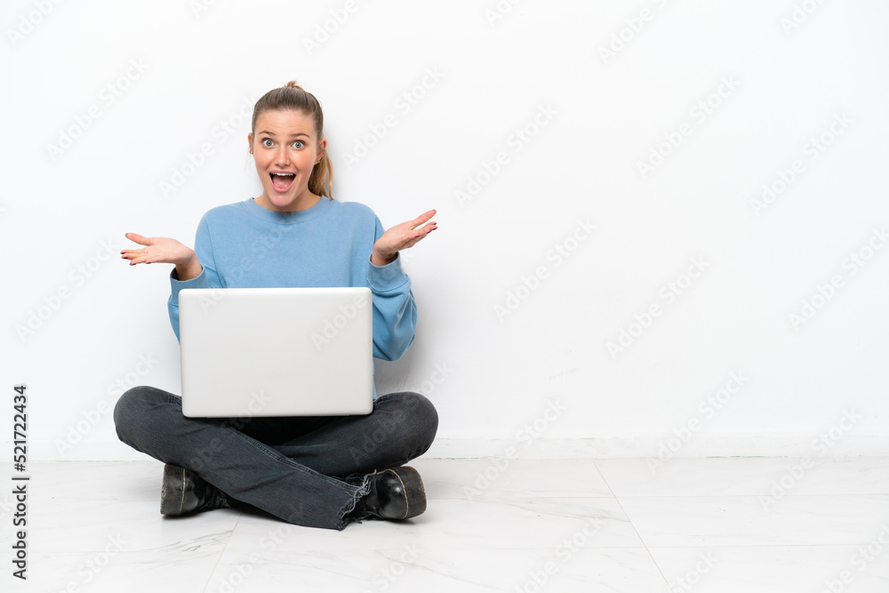Young woman with a laptop sitting on the floor with shocked facial expression