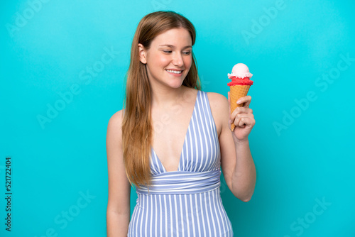 Young caucasian woman in swimsuit eating ice cream isolated on blue background with happy expression
