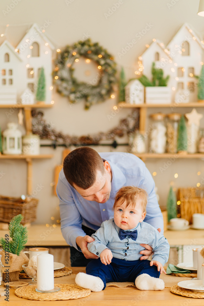 dad and baby son in the decorated for the new year kitchen. father's day dad and baby son in the decorated for the new year kitchen. father's day
