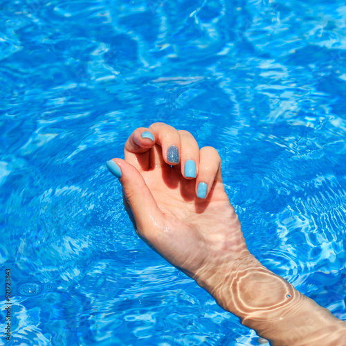 Close-up of female manicured hands. Woman's hands with bright glitter blue fingernails inside of bright blue swimming pool water.