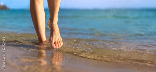 A woman walking on the beach shore with a blue ocean background.