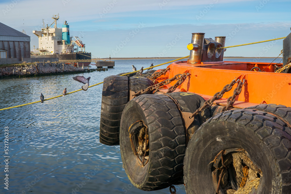 Close-up of anti-shock tires of a fishing boat and seaport in the background