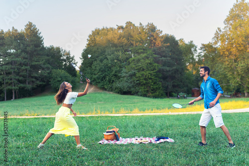 Young smiling couple playing badminton during picnic on the meadow photo