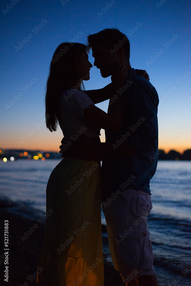 Silhouette of young couple in love hugging on the beach at summer sunset