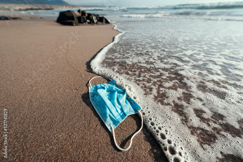 disposable face mask on the beach thrown away polluting the ocean and the planet