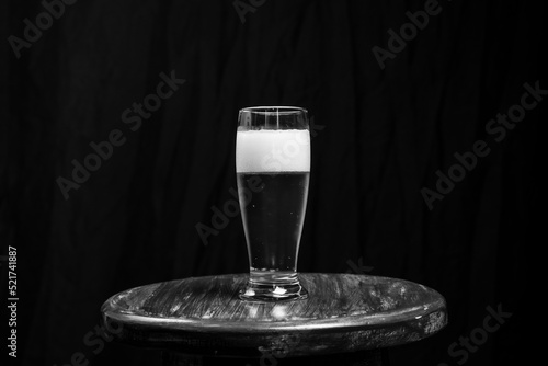 Studio Portrait of a glass cup with yellow liquid, on top of a wooden bench, against a black studio background. photo