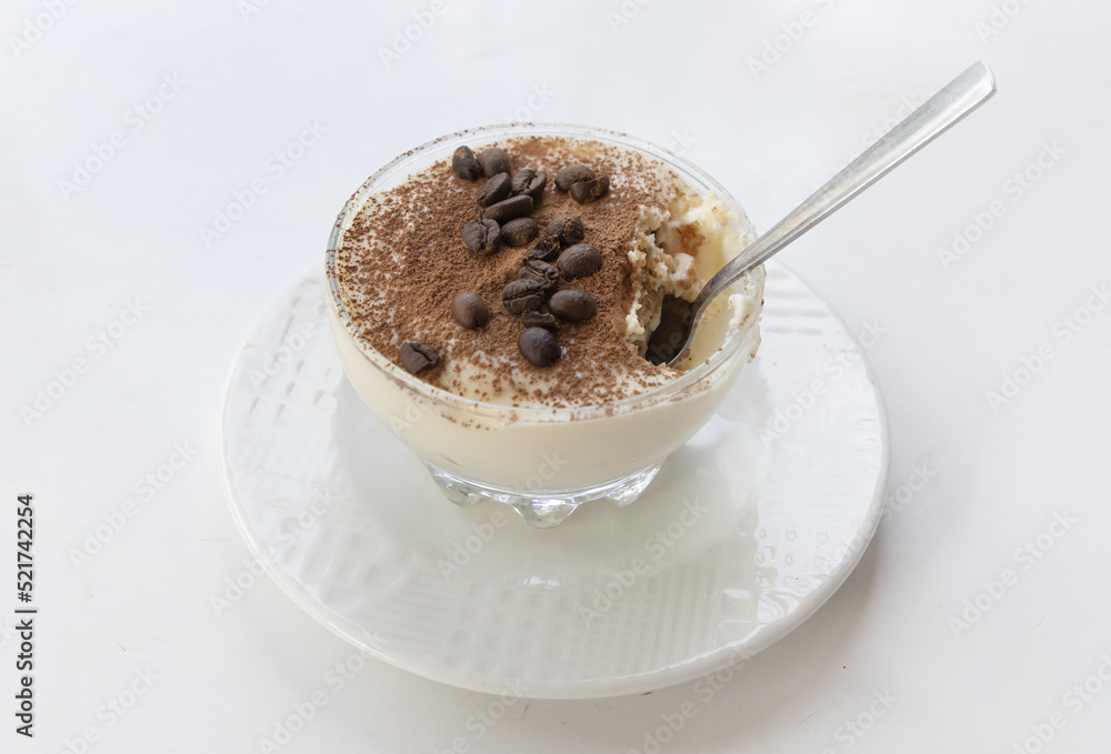 Dessert tiramisu with cocoa and coffee beans in a transparent bowl on a white table in an Italian cafe. Dessert tiramisu with cocoa and coffee beans in a transparent bowl on a white table in an Italian cafe.