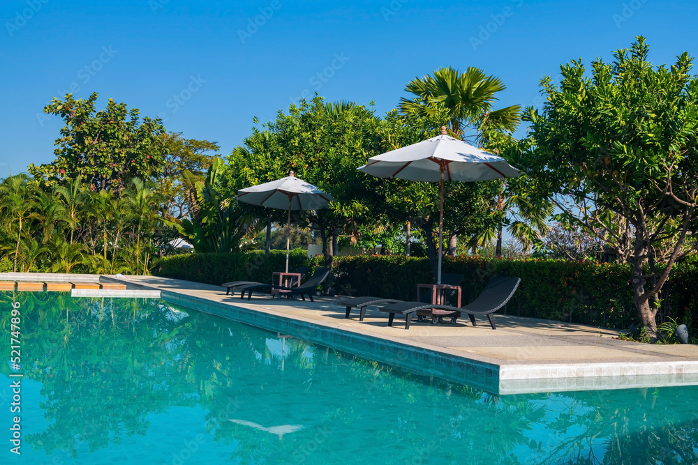 Fototapeta premium Empty sunbeds with parasols at swimming pool against blue sky