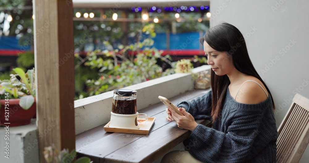 Woman look at mobile phone and drink of hot tea at outdoor coffee shop