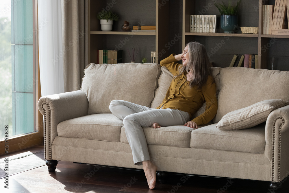 Happy beautiful grey haired elderly woman sitting on comfortable couch in living room, leaning on back, relaxing, thinking, dreaming with happy smile, enjoying leisure, being at home Happy beautiful grey haired elderly woman sitting on comfortable couch in living room, leaning on back, relaxing, thinking, dreaming with happy smile, enjoying leisure, being at home